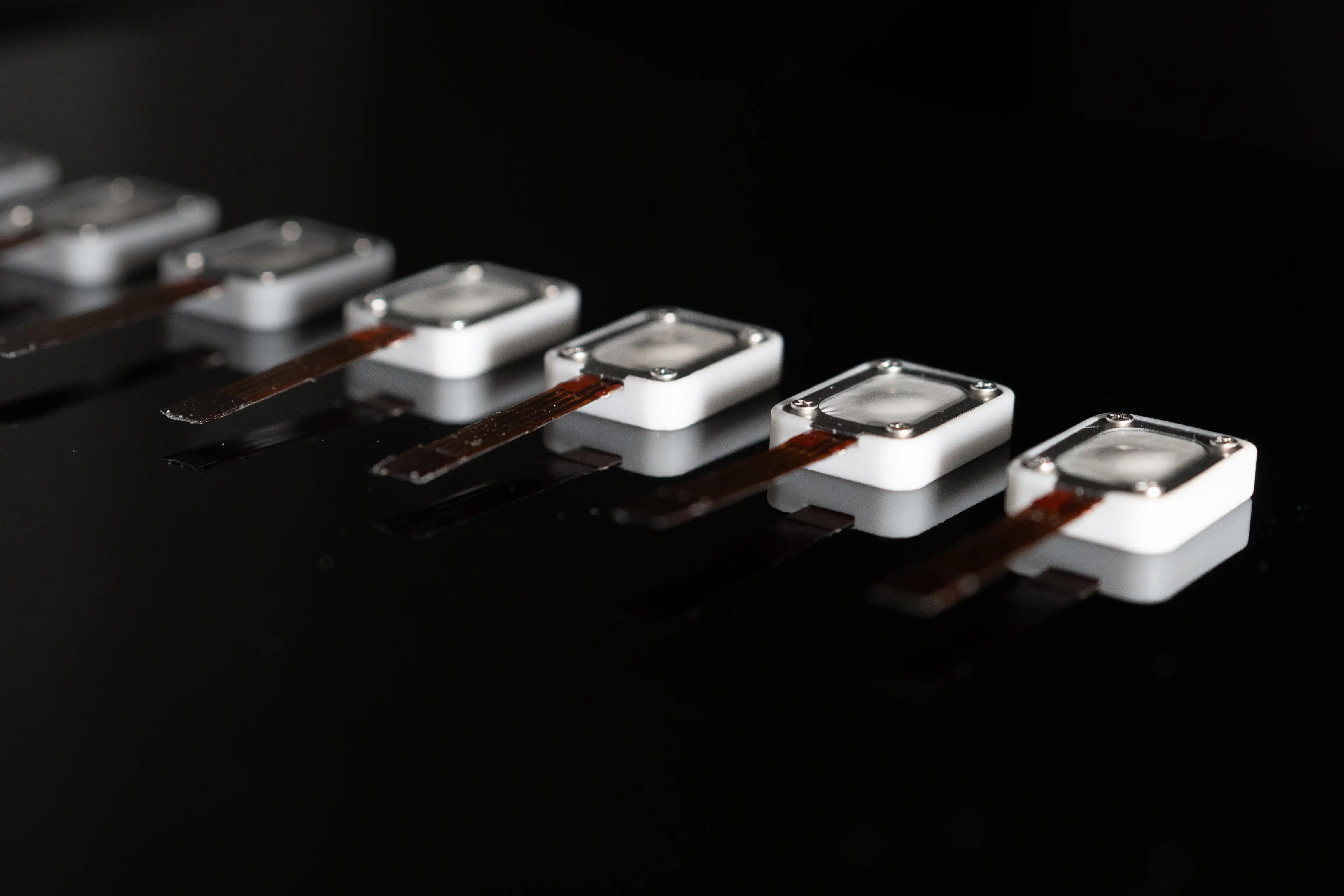 Row of electroosmotic haptic actuators on black glass, macro photograph